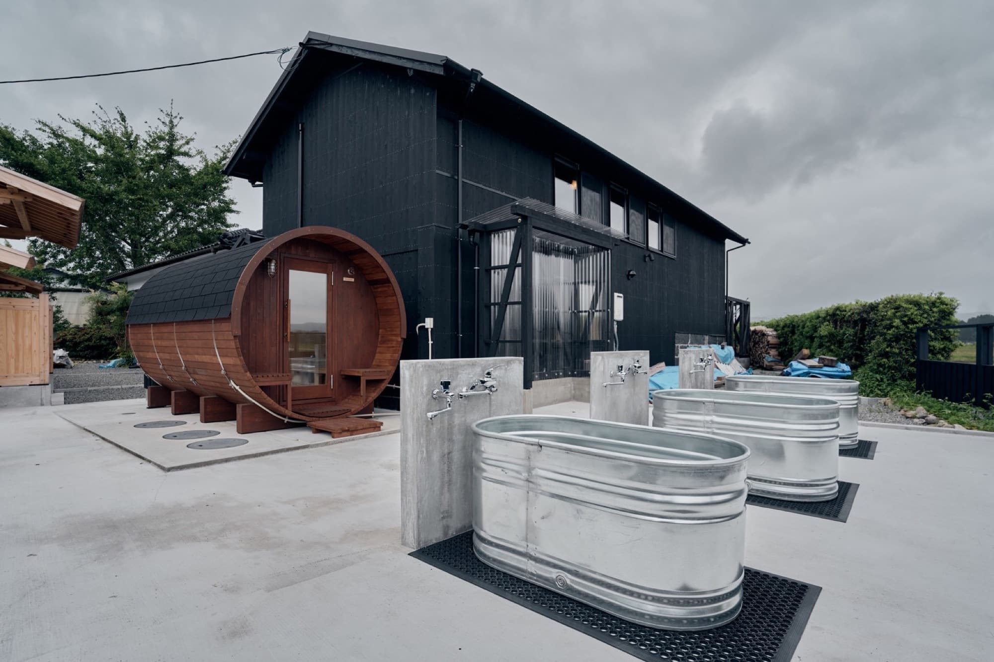 The cedar barrel sauna and galvanized cold-plunge tubs beside the black house